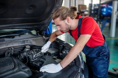 İngiliz anahtarı olan bir adam arabanın kaputuna yaslanmış.