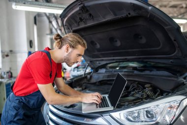 Arabanın kaputu açık dizüstü bilgisayarı olan adam.