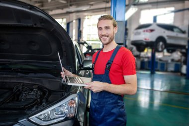 Arabanın kaputunun yanında dizüstü bilgisayarı olan bir tamirci.