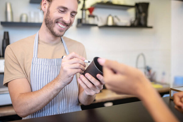 Smiling man in apron writing with marker on glass