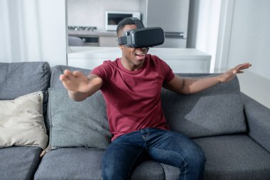 Siyah tenli genç bir adam VR gözlükleriyle oturuyor ve eğleniyor.