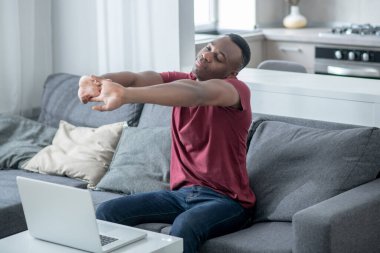 Afrikalı Amerikalı genç adam kanepede oturuyor ve esniyor.