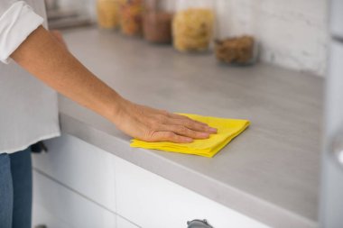 Masanın yüzeyini sarı bir ev örtüsüyle silen kadın.