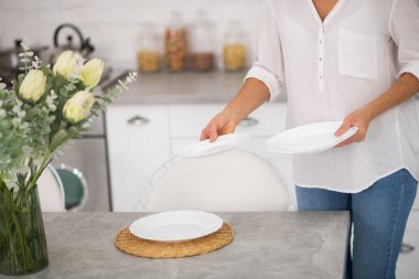 Gömlekli ve kot pantolonlu ev hanımı akşam yemeği için masaya servis yapıyor.