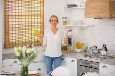 Kotlu ve gömlekli sarışın kadın mutfağı dezenfekte ediyor.