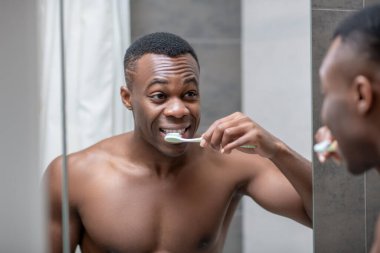 Afrikalı Amerikalı genç yakışıklı adam dişlerini temizliyor.