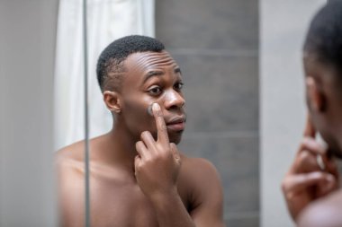 Afrikalı kısa saçlı adam yüzüne krem sürüyor.