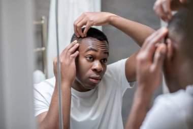 Beyaz tişörtlü Afro-Amerikan adam saçını yapıyor.