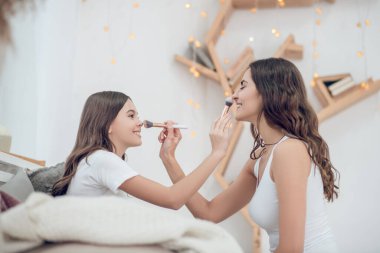 Anne ve kızı birbirlerine makyaj yapıyorlar.