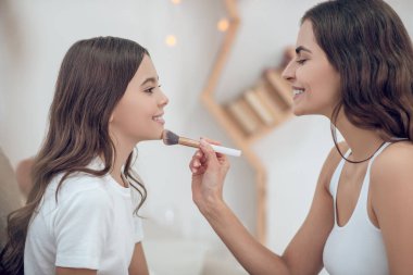 Makyajlı anne genç kızın çenesine dokunuyor.