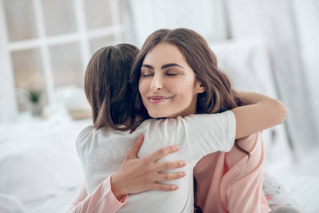 Happy mom with closed eyes hugging daughter tightly