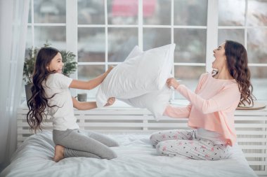 Anne ve kızı yatakta yastık savaşı yapıyor.