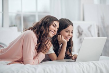 Annesinin kucak dolusu kızı dizüstü bilgisayar ekranına bakıyor.