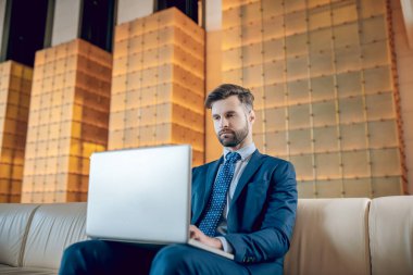 Takım elbiseli sakallı bir adam dizüstü bilgisayarda çalışıyor ve konsantre görünüyor.