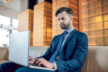 Takım elbiseli sakallı bir adam dizüstü bilgisayarda çalışıyor ve konsantre görünüyor.