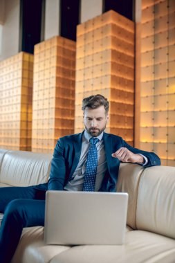 Takım elbiseli sakallı bir adam dizüstü bilgisayarda çalışıyor ve konsantre görünüyor.