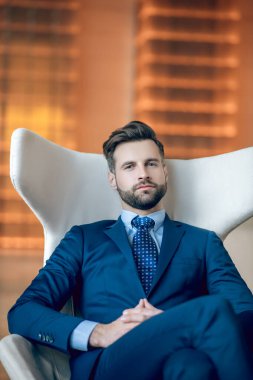 Takım elbiseli bir adam koltukta oturuyor ve tatminsiz görünüyor.