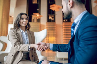 Bej takım elbiseli bir kadın iş ortağıyla el sıkışıyor.