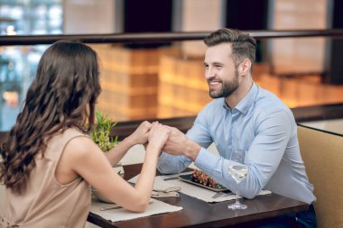 Restorandaki masada oturan bir çift ve kadınların elini tutan bir adam.