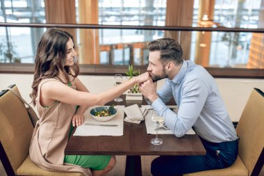 Restorandaki masada oturan bir çift ve kadınların ellerini öpen bir adam.