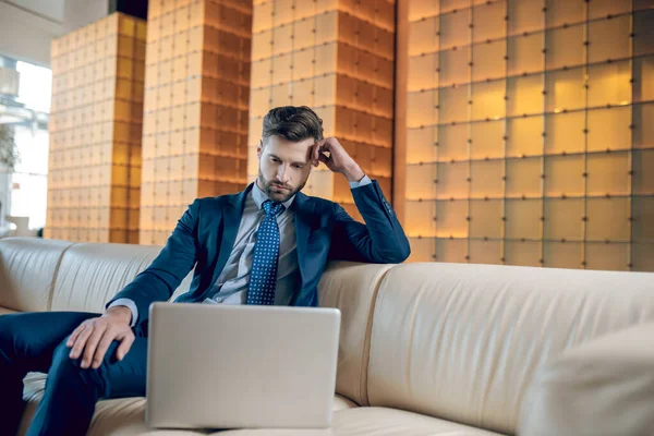 Takım elbiseli sakallı bir adam dizüstü bilgisayarda çalışıyor ve konsantre görünüyor.