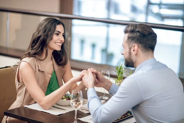 Restorandaki masada oturan bir çift ve kadınların elini tutan bir adam.