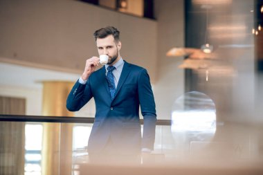 Güzel takım elbiseli şık bir işadamı kahve içiyor.