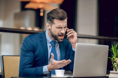 Mavi takım elbiseli bir iş adamı telefonda konuşuyor ve kızgın görünüyor.