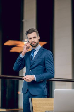 Mavi takım elbiseli bir iş adamı telefonda konuşuyor ve olaya dahil gibi görünüyor.