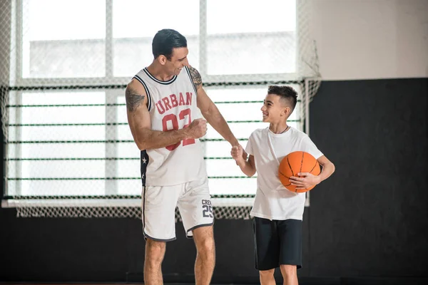 Coach in white sportswear teaching the boy playing basketball