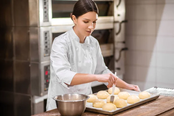 Pişirmeden önce çöreğe krema süren kadın. — Stok fotoğraf