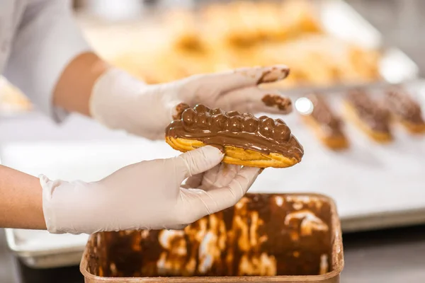 Patissiers Hände halten Eclair in Schokolade Topping — Stockfoto