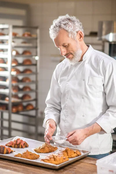 Pria berseragam yang mendekorasi croissant siap pakai — Stok Foto