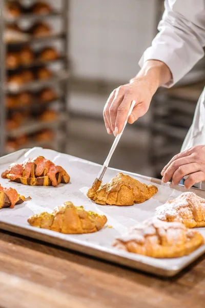 Pastry chefs hand with brush over tray of croissants — Stock Photo, Image