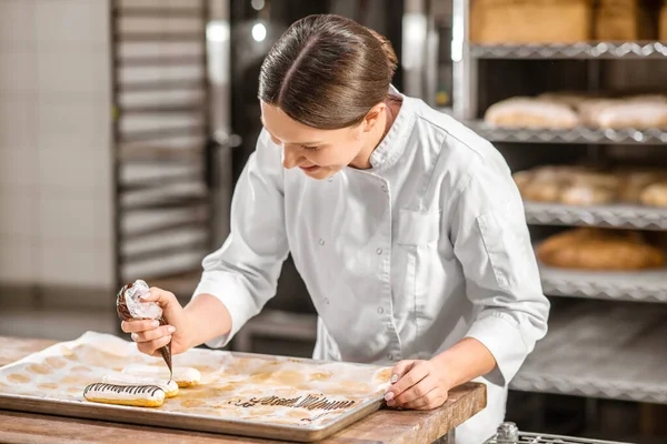 Woman decorating surface of finished eclairs — Stock Photo, Image