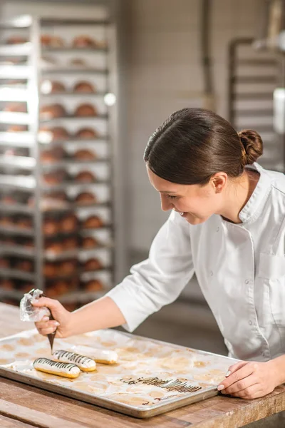 Mujer experimentada pastelería chef hábilmente decorar eclairs —  Fotos de Stock