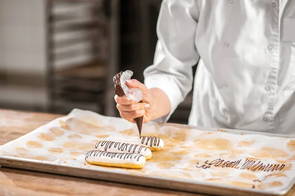 Pasteleros mano apretando bolsa de pastelería sobre eclair —  Fotos de Stock