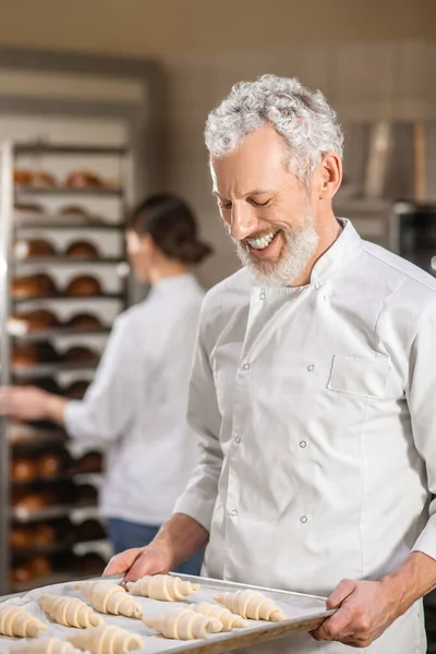 Happy man looking at tray of croissants and woman — Stock Photo, Image