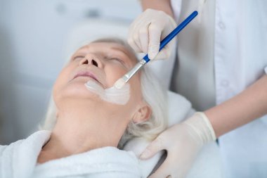 Kozmetik uzmanı kadınların yüzüne nemlendirici maske takıyor.