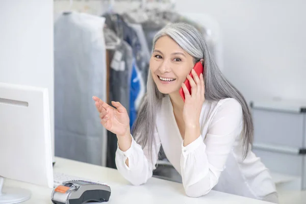 Glada kvinna vid disken talar på smartphone — Stockfoto