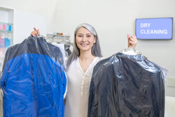 Woman standing in dry cleaning showing suits