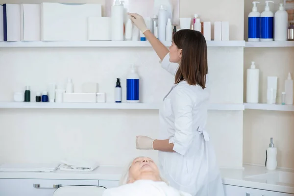 Cosmetoloog in een witte jas die schoonheidsproducten uit de kast haalt — Stockfoto
