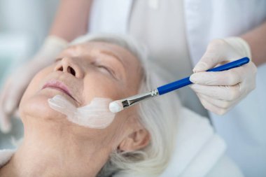 Kozmetik uzmanı kadınların yüzüne nemlendirici maske takıyor.