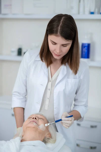 Cosmetoloog het aanbrengen van hydraterende masker op de vrouwen gezicht — Stockfoto