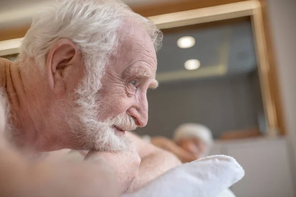 Homem idoso de cabelos grisalhos deitado em um sofá e esperando por massagem nas costas — Fotografia de Stock