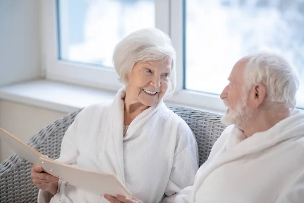 Старшая пара в белых халатах выбирает процедуры в спа-центре и наслаждается видом — стоковое фото