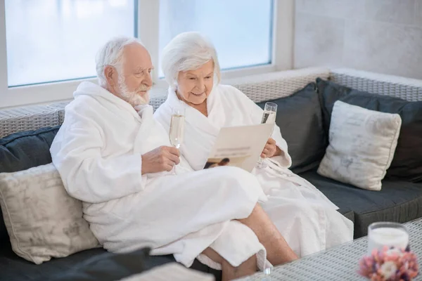 Pareja mayor vestida con túnicas blancas pasándola muy bien en el salón de spa y luciendo relajada — Foto de Stock