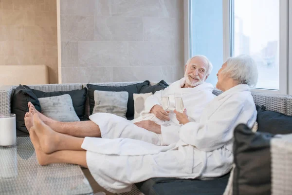 Casal sênior em vestes brancas tendo ótimos momentos no salão de spa e olhando relaxado — Fotografia de Stock