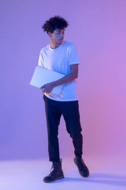 Beyaz tişörtlü, laptoplu kıvırcık saçlı genç adam.