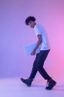 Koyu tenli, beyaz tişörtlü, dizüstü bilgisayarı olan bir genç.